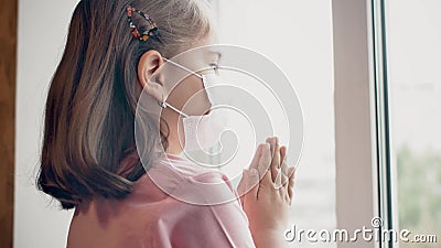 A little girl in medical mask pray for good health near the window Stock Photo