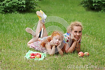 Little girl and mother lie on lawn in green summ Stock Photo