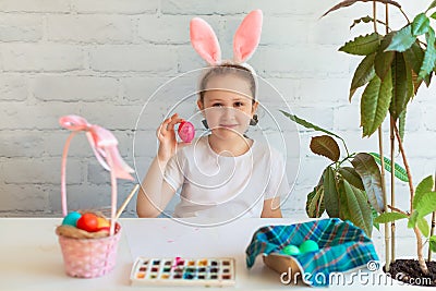 Little Girl paints eggs for Easter Holiday Baby Wears Rabbit ears on Easter Day. Stock Photo