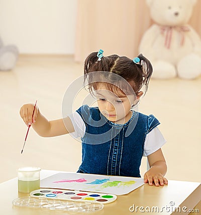 Little girl paints with watercolors at the table. Stock Photo