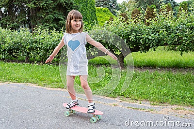 Little girl in the park learns to ride a skateboard Stock Photo