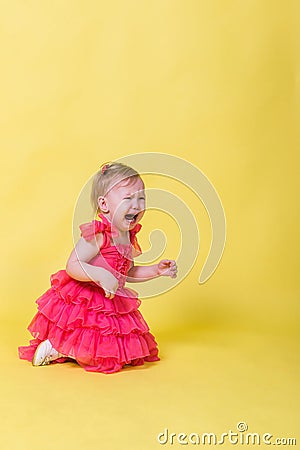 Little girl in pink dress kneeling and crying on a yellow background Stock Photo