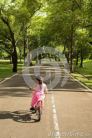 The little girl in pink dress trying to ride a bike headed for a narrow street in the park. Stock Photo