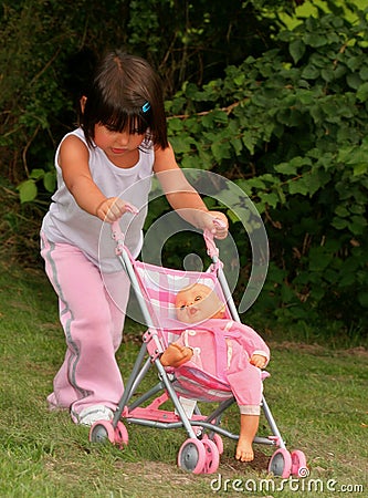 Little Girl in Pink Pushing a Dolly in a Pram. Stock Photo