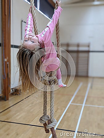 Little girl in pink swinging from ropes in the school gymnasium Stock Photo