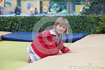 Little girl on playground in a park, jumping on trampoline. Little Girl seating on a Trampoline Stock Photo