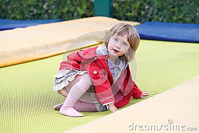 Little girl on playground in a park, jumping on trampoline. Little Girl seating on a Trampoline Stock Photo