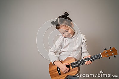 Little girl plays ukulele. Creative development in children. Musical education from childhood. Teaching music online at home Stock Photo