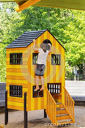 Little girl with pony tail and sandy feet climbs playhouse on playground in the Gathering Place public park in Tulsa OK Editorial Stock Photo