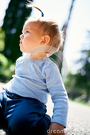Little girl with a ponytail sits on her knees on the road. Close-up Stock Photo