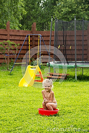 Little girl in the rain in a red basin on grass Stock Photo