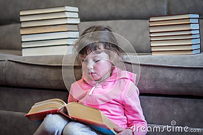 A little girl is reading a big, fat book in her lap. Serious child is studying a textbook. Children`s educational concept Stock Photo
