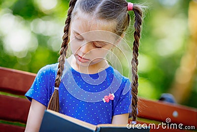 Little girl reading a book in the outdoors. Stock Photo