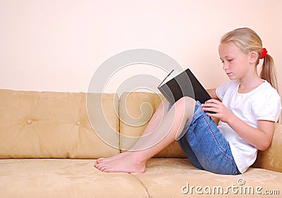 Little girl reading book on sofa Stock Photo