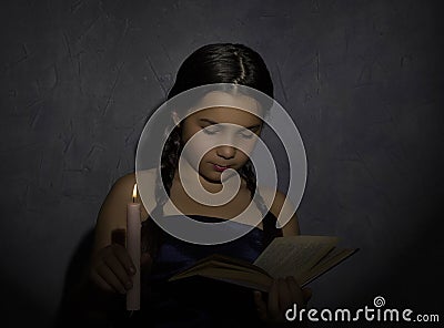 Little girl reading book and studying in candle light in dark room Stock Photo