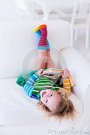 Little girl reading a book on a white couch Stock Photo