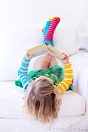 Little girl reading a book on a white couch Stock Photo