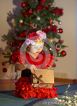 Little girl in red dress opens a present near the Christmas tree Stock Photo