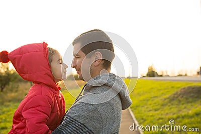 A little girl in a red jacket with a hood hugs and kisses her dad, smiles, touches her nose. Happy family, father`s day, bright ra Stock Photo