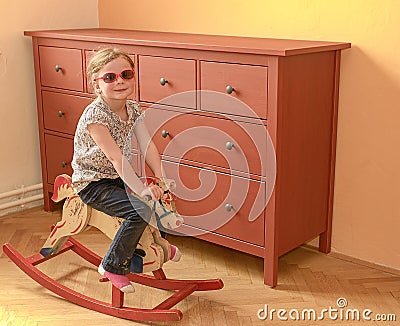 Little girl on rocking horse. Small girl wears red glasses. Stock Photo