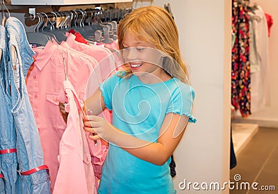 Little girl shopping in clothes store. Child chooses dress at clothes shop. Stock Photo