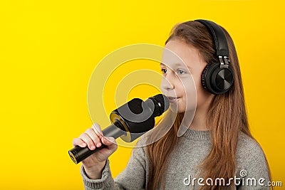 Little girl sings into a microphone on a yellow background. Karaoke for children Stock Photo