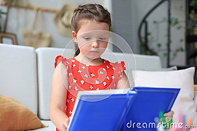 Little girl sits at the desl at home and does homework, self study of the material, reading book Stock Photo