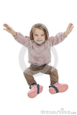 A little girl sits and laughs with her hands up. Cute child in brown jeans and a pink sweater. Happiness, positivity and joy. Stock Photo