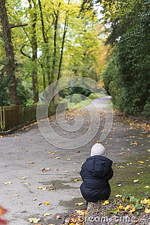 Little girl sitting on a footpath in the park in autumn Stock Photo