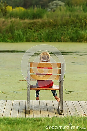 Little girl sitting in a giant wooden chair on the lake bank Stock Photo