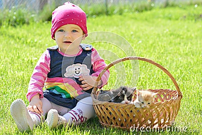 Little girl sitting in green grass with three kittens in basket Stock Photo