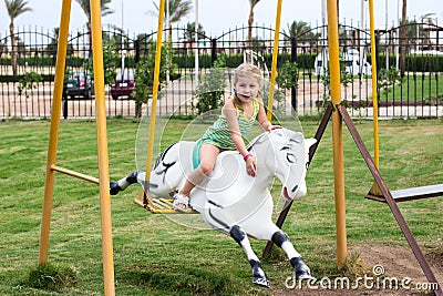 Little girl sitting on harseback of children swing, swinging on playground Stock Photo