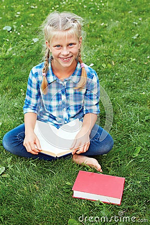 Little girl is sitting reading on the grass. Stock Photo