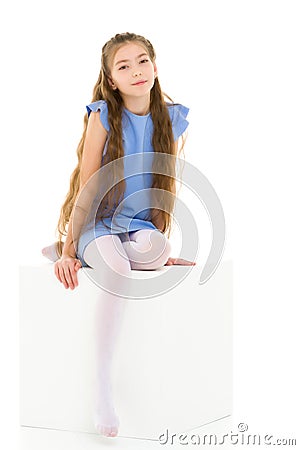 Little girl sitting on a white cube cross-legged. Stock Photo