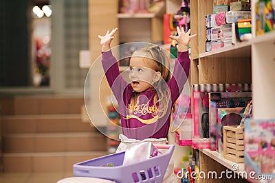 Little girl with small shopping cart in kids mall. Happy girl choosing what to buy in toy store Stock Photo
