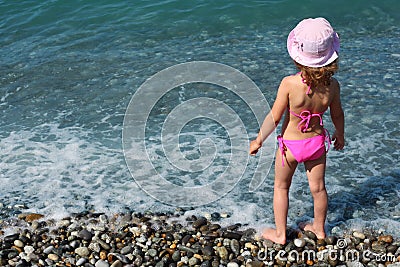 Little girl stands on beach, rear view Stock Photo