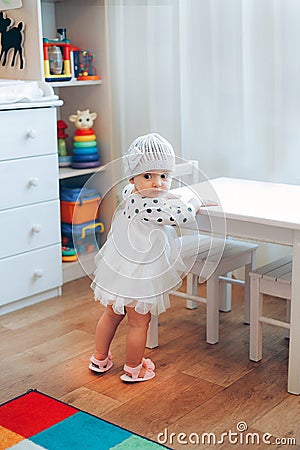 A little girl standing near a white table in a dress with black polka dots Stock Photo