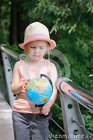 Little girl in a straw panama. Child considers the model of the globe. Stock Photo