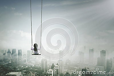 Little girl with swing above misty city Stock Photo