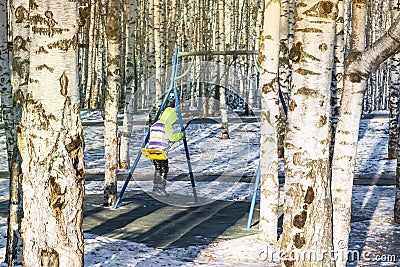 Little girl swinging on a swing in a city Park in winter on a background of birch trunks Editorial Stock Photo