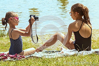 Cute little girl sitting on the grass on sunny summer day and taking picture with camera. Summer holidays.Little girl taking Stock Photo