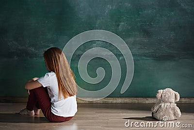 Little girl with teddy bear sitting on floor in empty room. Autism concept Stock Photo