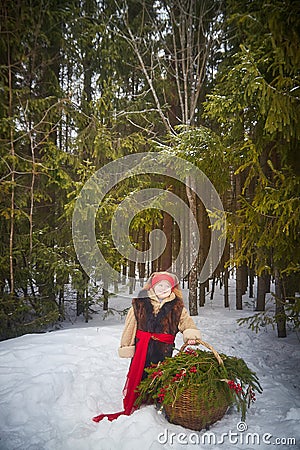 Little girl in thick coat and a red sash with basket of fir branches and red berries in cold winter day in forest Stock Photo