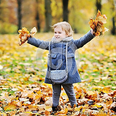 Little girl tossing leaves in autumn park Stock Photo