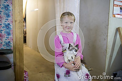 A little girl in a traditional dress stands with a kitten in her hands in the house Editorial Stock Photo