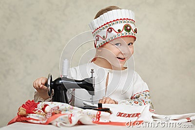 Little girl in the traditional russian shirt and kokoshnik at the process of sewing Stock Photo