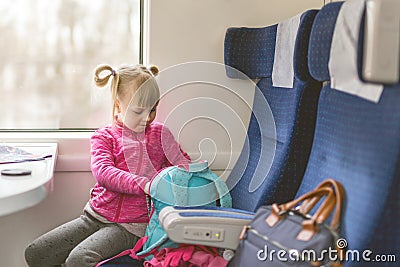 Little girl travel by train. Kid sitting in comfortable chair and looking in backpack. Things to take with on railroad trip with Stock Photo
