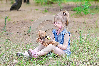A little girl treats her teddy bear in a forest glade a copy of Stock Photo