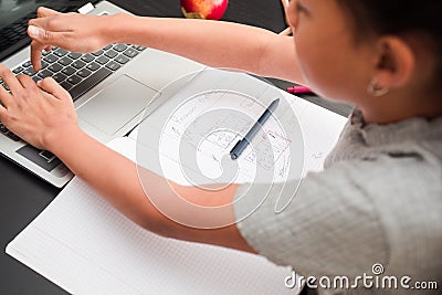 Little girl typing on the laptop. Detail of schoolchild taking notes and using the laptop on the black desk Stock Photo