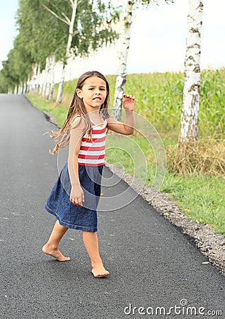 Little girl walking barefoot on asphalt street Stock Photo